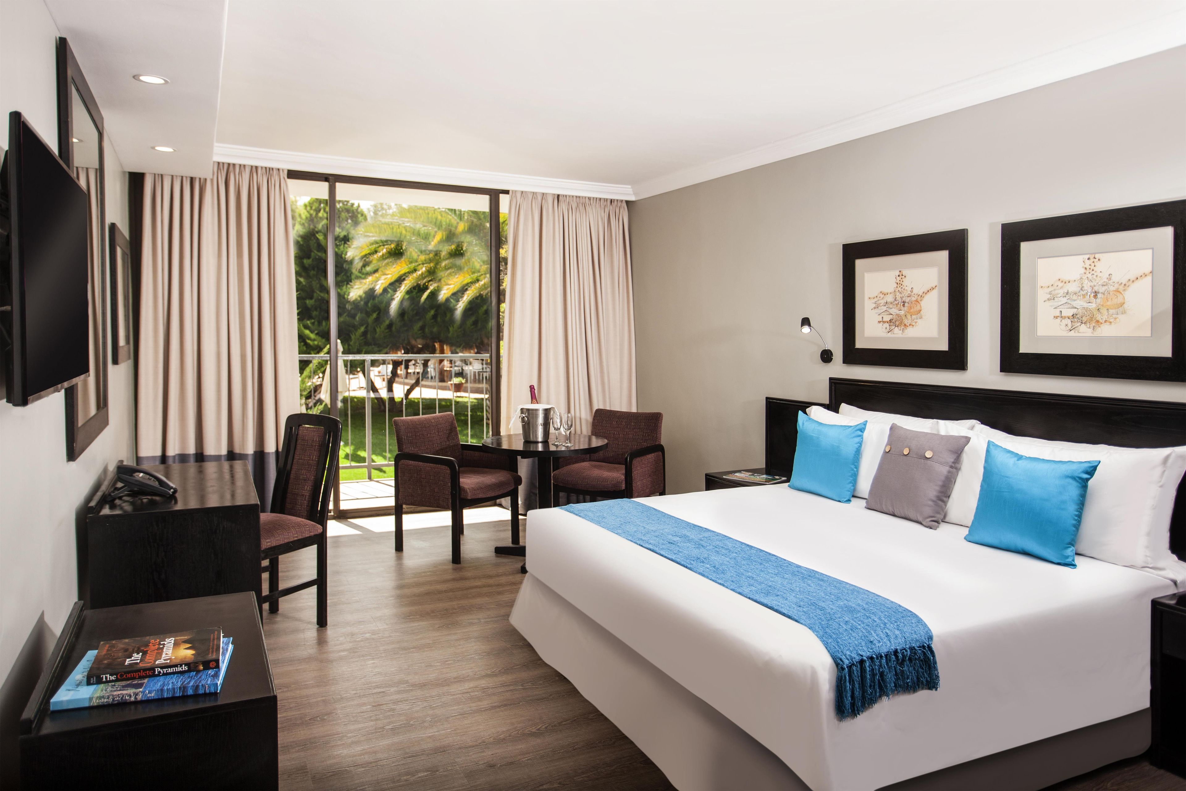 Una habitación de hotel con una cama grande, un escritorio con una silla, un televisor y obras de arte en las paredes.