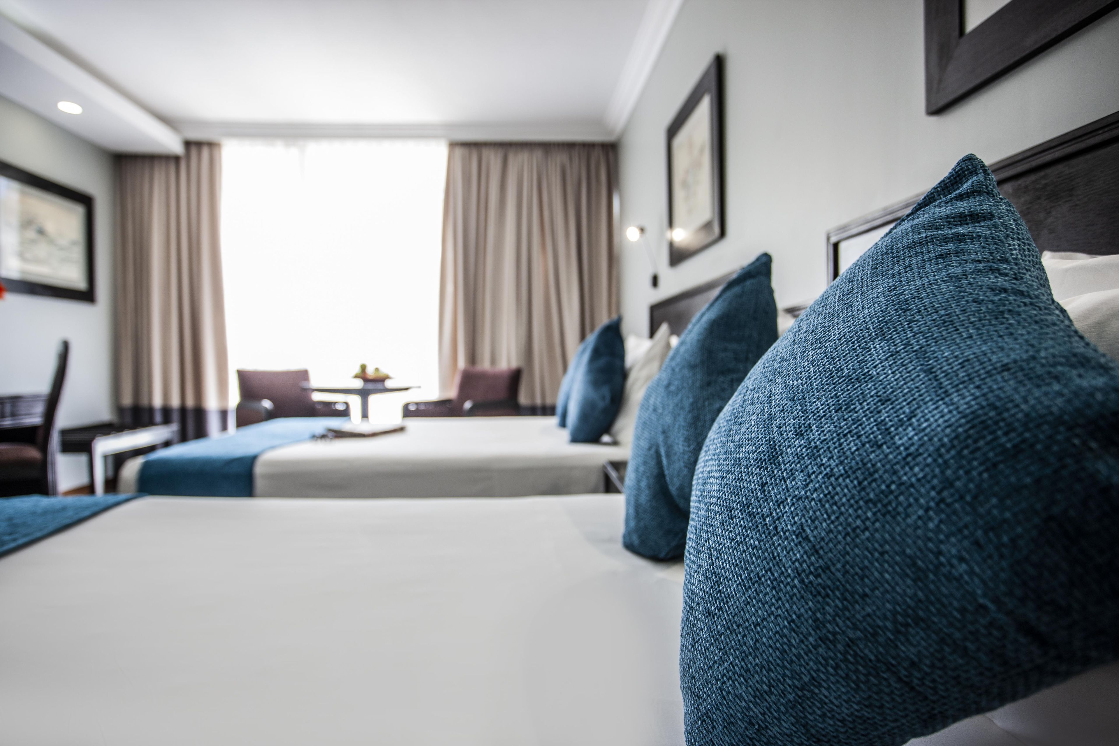 A hotel room with a bed, two pillows, a desk, a chair, and a window with curtains.