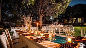 An outdoor dining setup with tables set for a meal, surrounded by trees and string lights. - Avani Maseru Hotel (Maseru)