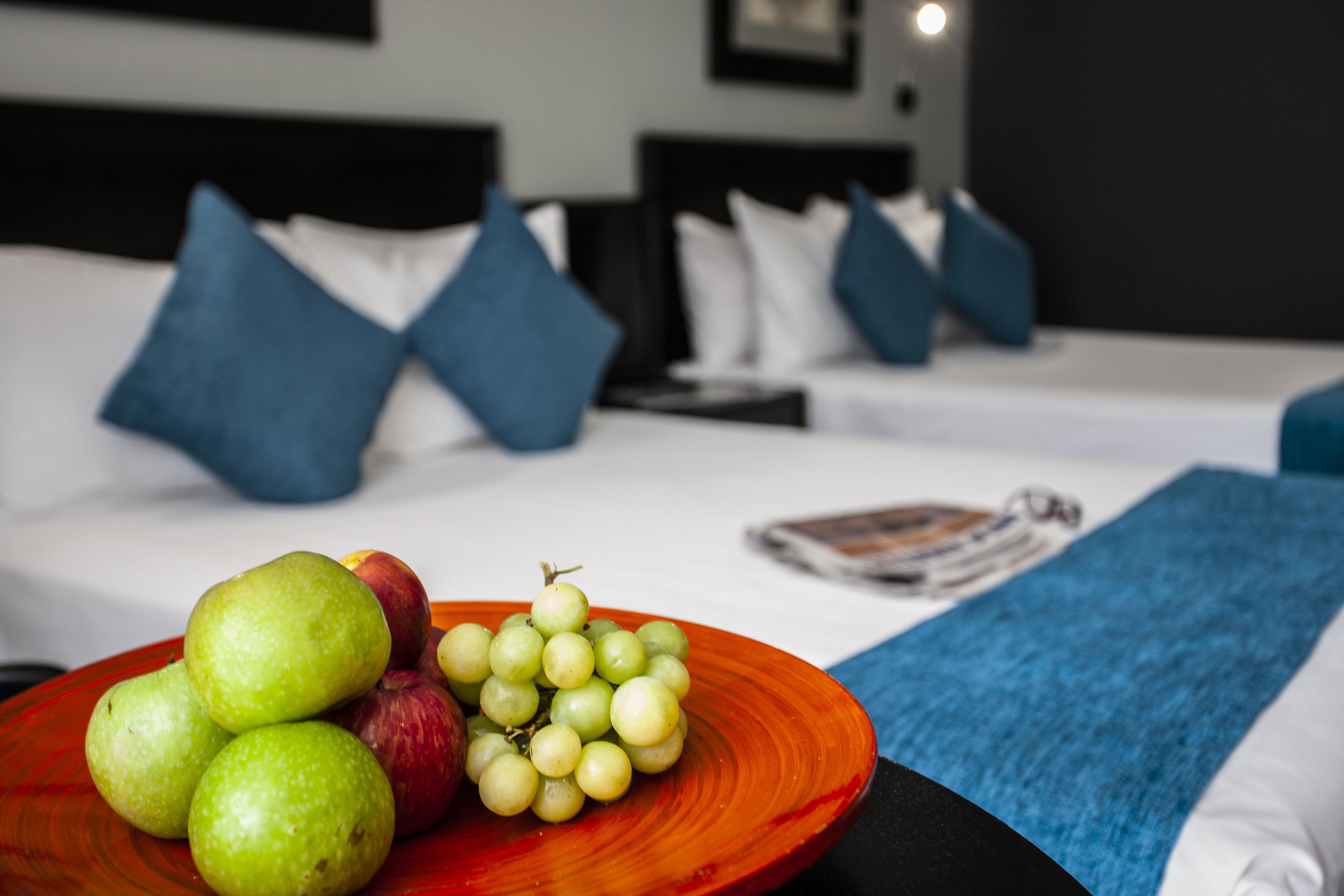 A hotel room with a bed, pillows, a magazine, and a plate of fruit.