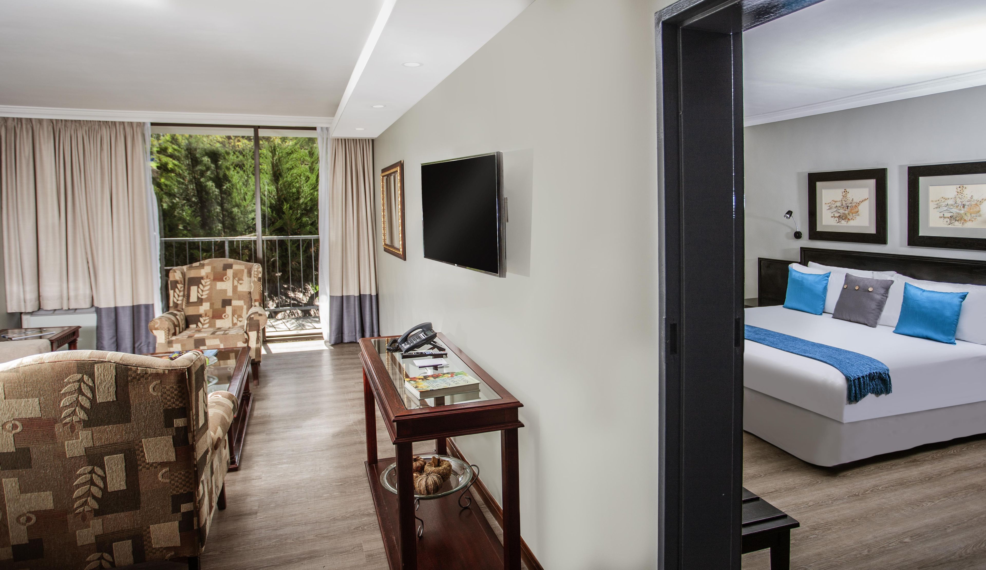 Habitación de hotel con cama, escritorio con teléfono, silla, televisor y ventana con cortinas.