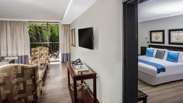 Habitación de hotel con cama, escritorio con teléfono, silla, televisor y ventana con cortinas.