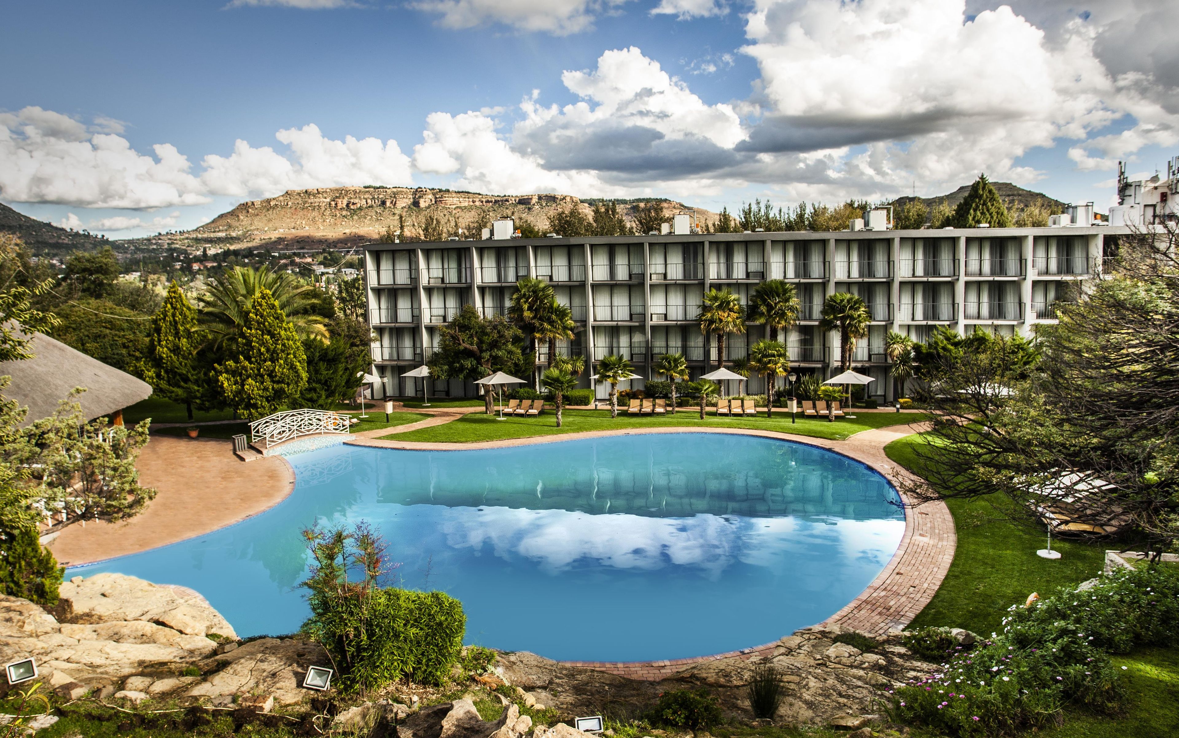 A hotel with a large swimming pool, multiple balconies, and a mountainous backdrop.
