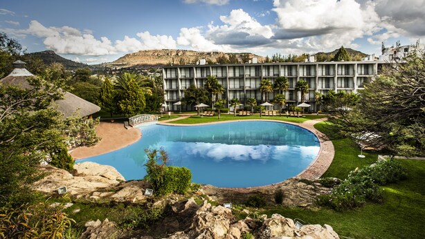 A hotel with a large swimming pool, lush greenery, and a mountainous backdrop. - Avani Maseru Hotel (Maseru)