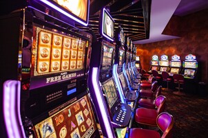 Una hilera de máquinas tragamonedas en un casino con sillas rojas al frente.
