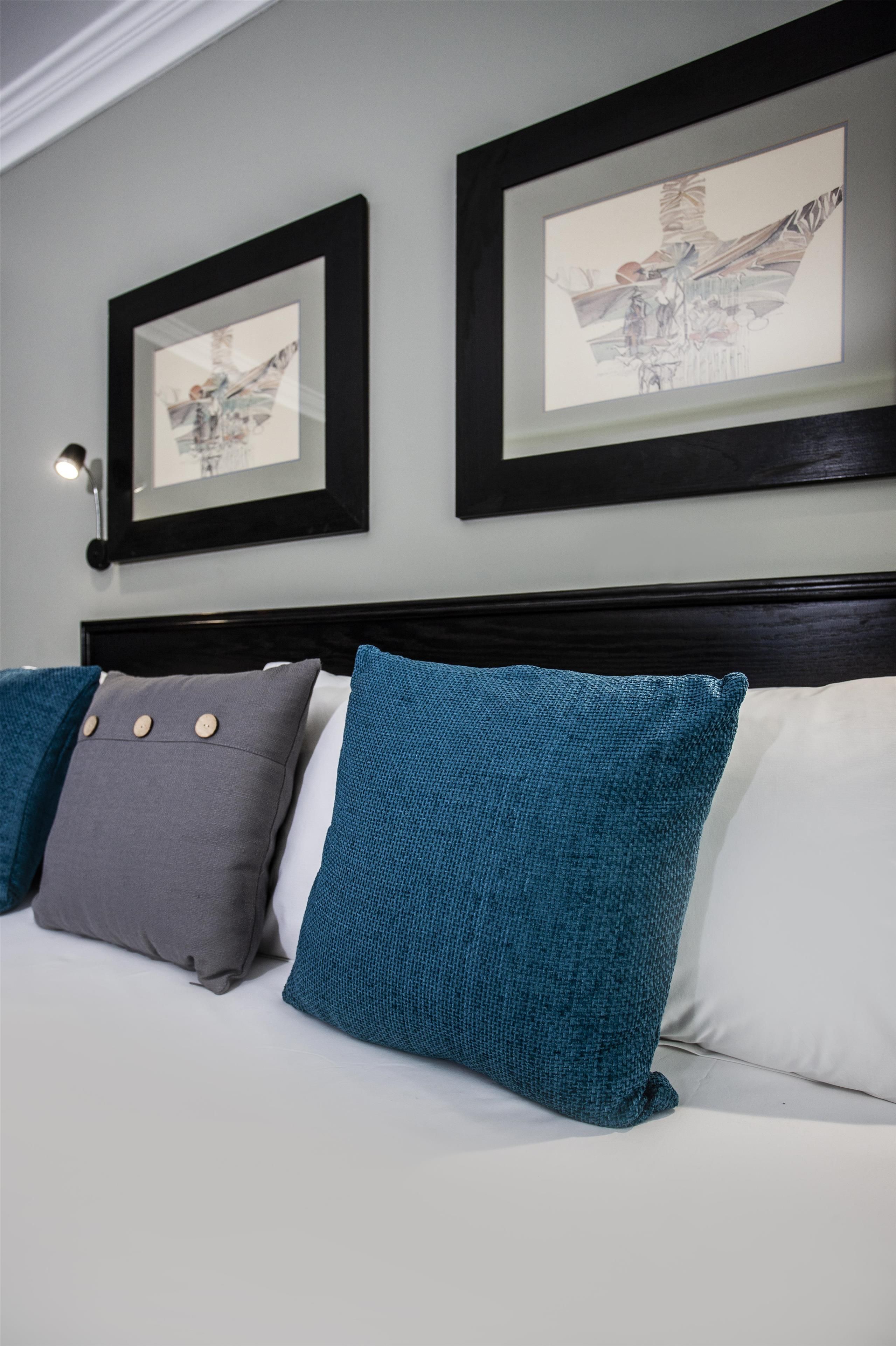 A bed with three pillows and two framed artworks on the wall.