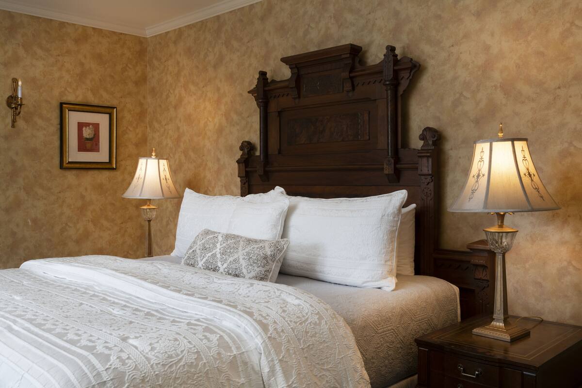 A neatly made bed with a white and beige bedspread, two bedside lamps, and a framed picture on the wall.