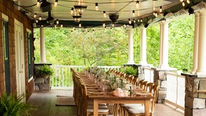 A covered outdoor dining area with a long wooden table set for a meal, surrounded by chairs, and string lights overhead. - The Inn at Thorn Hill & Spa (Jackson)