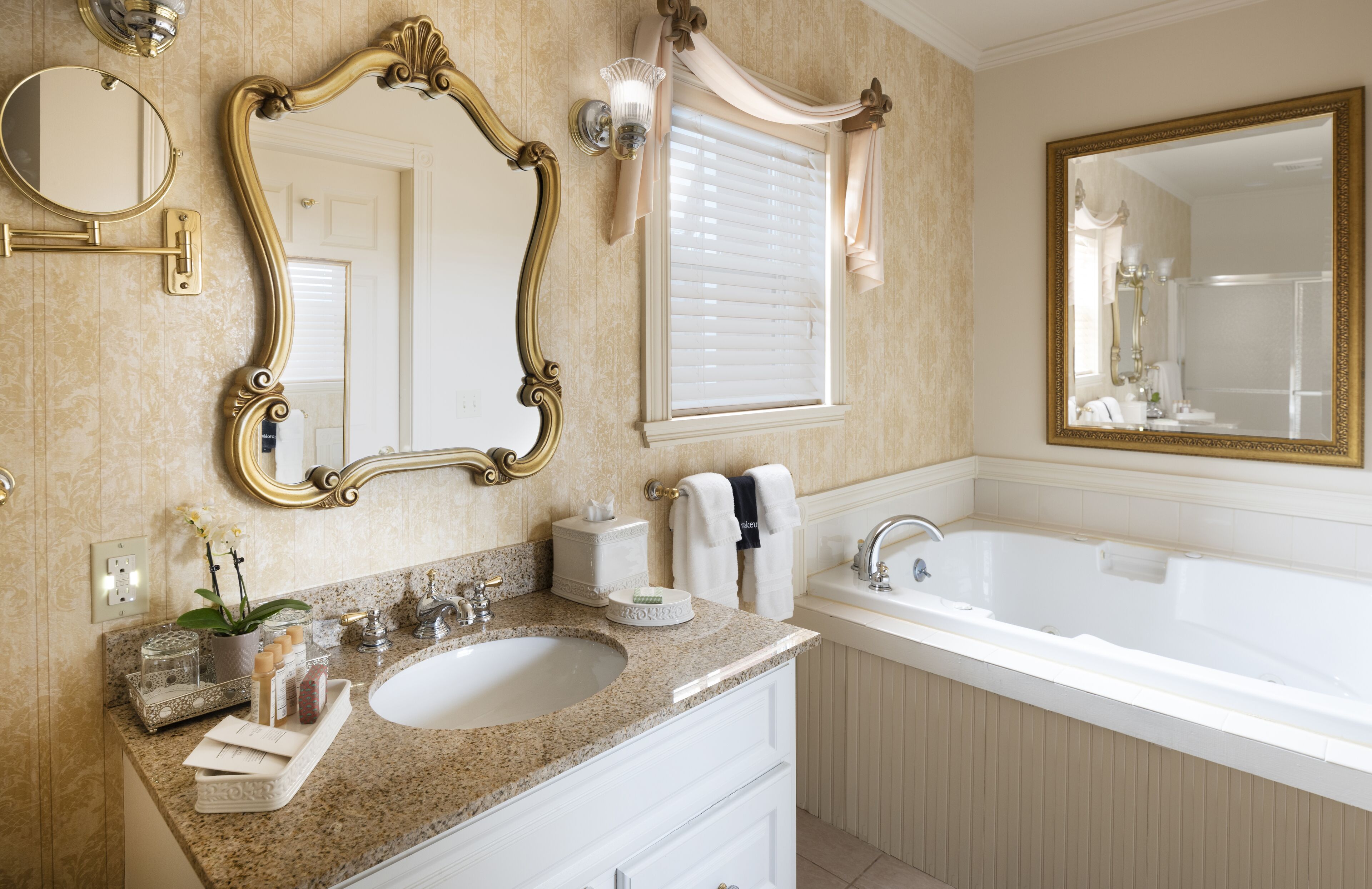 A bathroom with a double sink, vanity, large mirror, and bathtub.