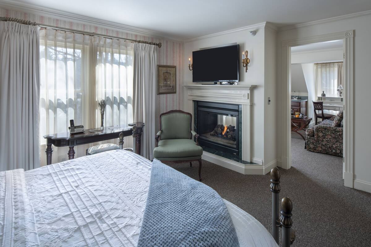A hotel room with a large bed, a fireplace, a television mounted above it, and a view into another room.