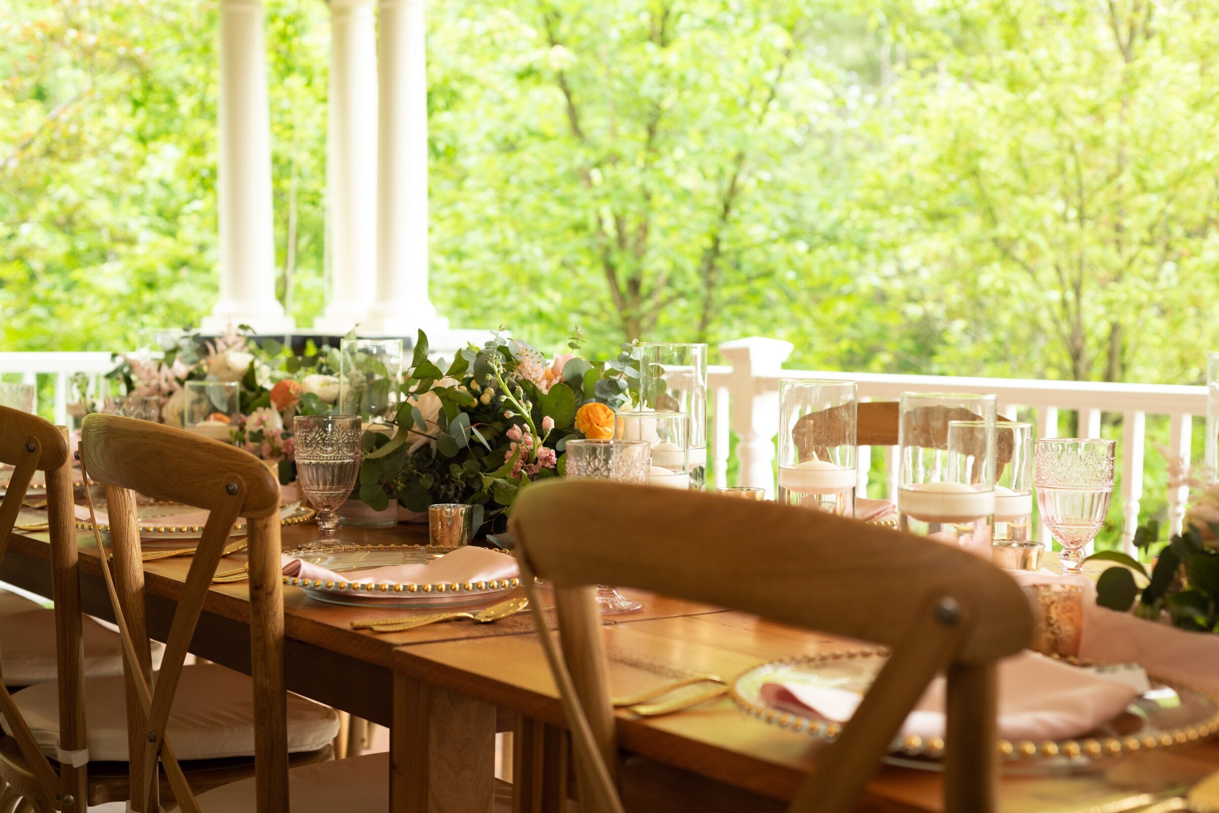 Una mesa de comedor al aire libre con sillas, cristalería y un centro de mesa floral.