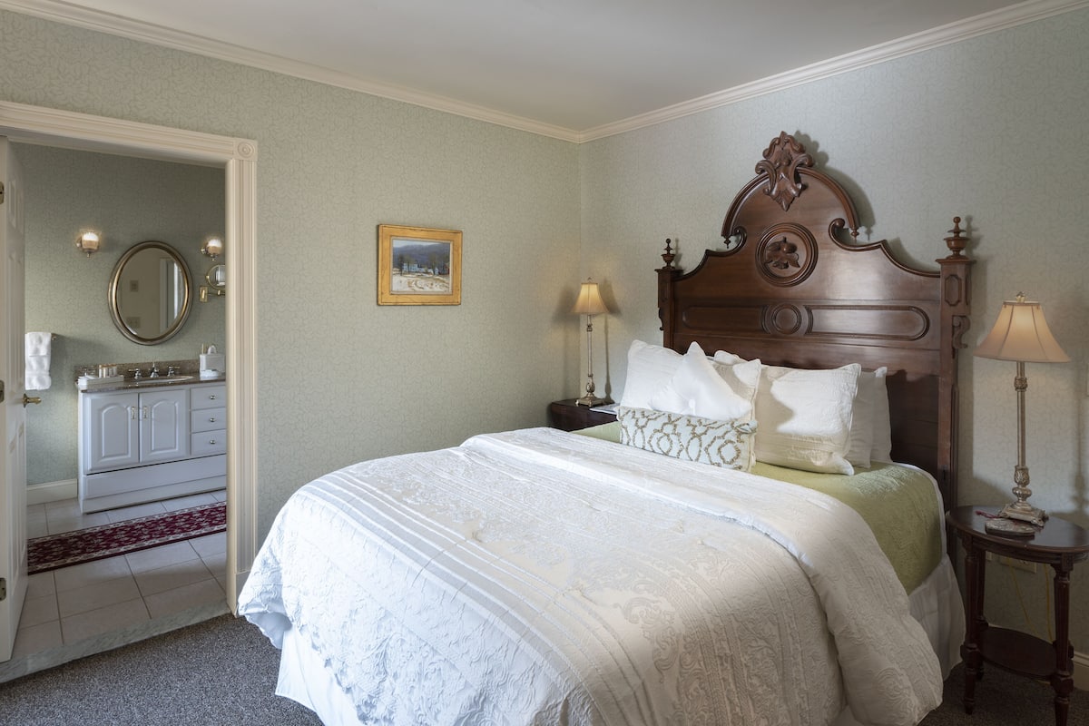 A neatly made bed with a wooden headboard, a bedside table with a lamp, and a framed picture on the wall.