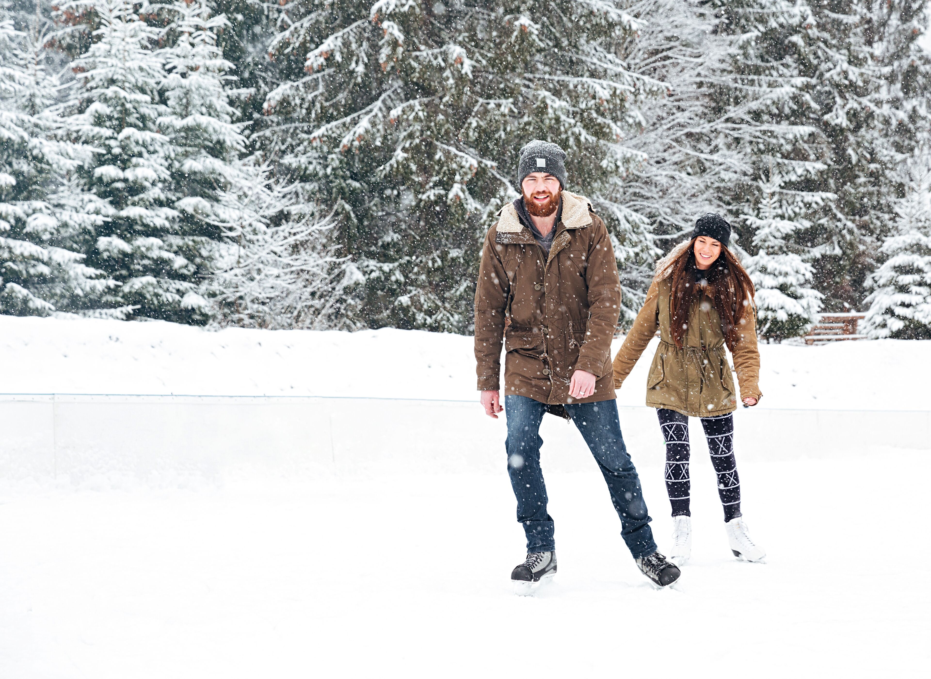 A couple holding hands in a snowy outdoor setting with snow-covered trees in the background.