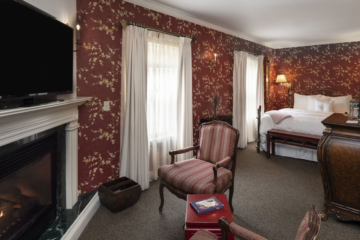 A hotel room with a fireplace, a television, a bed, a chair, and a desk.
