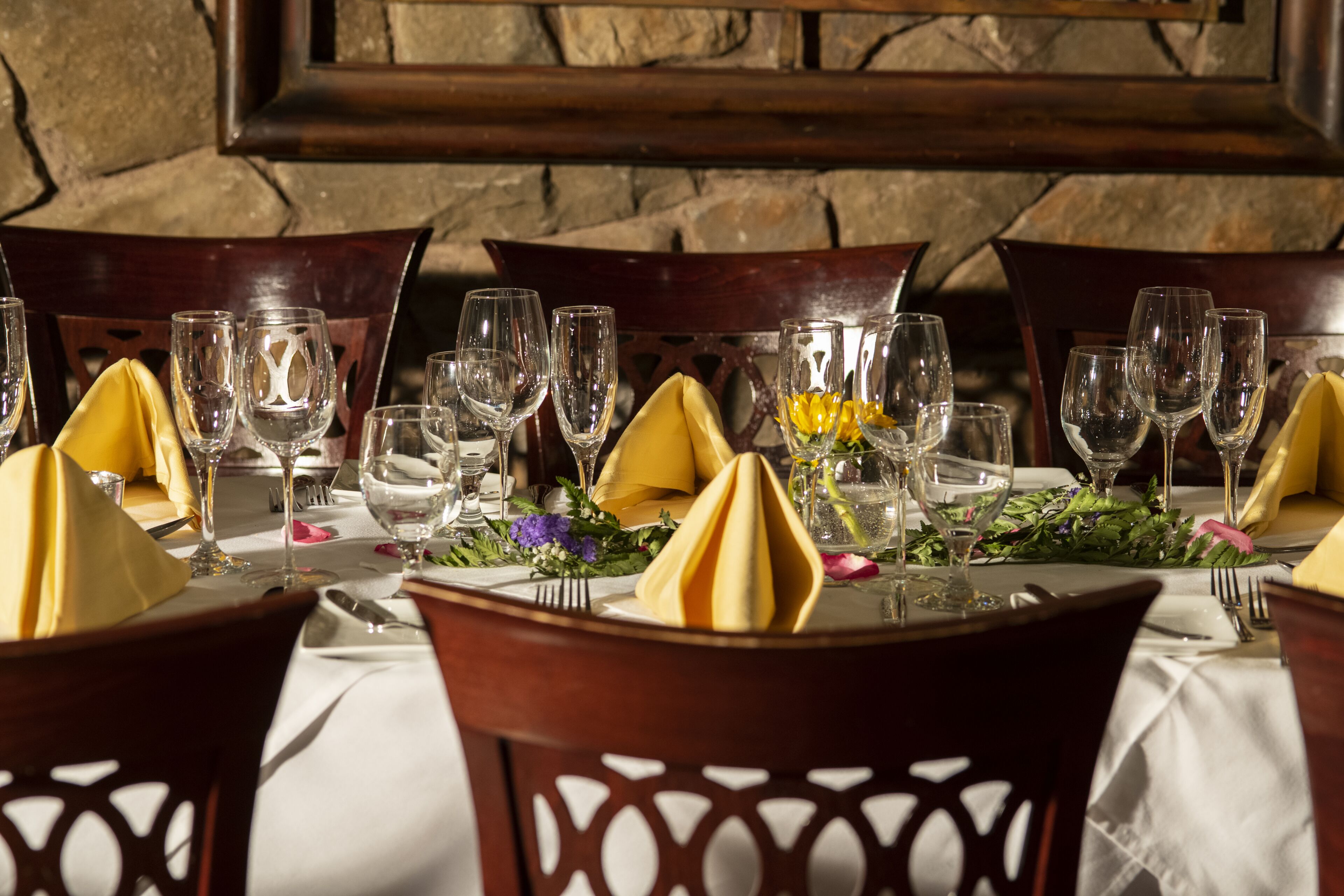 Mesa preparada para comer con varias sillas, un fondo de pared de piedra y techo de madera.