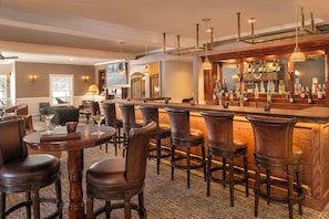 A bar area with wooden bar stools, a bar counter, and a variety of bottles.