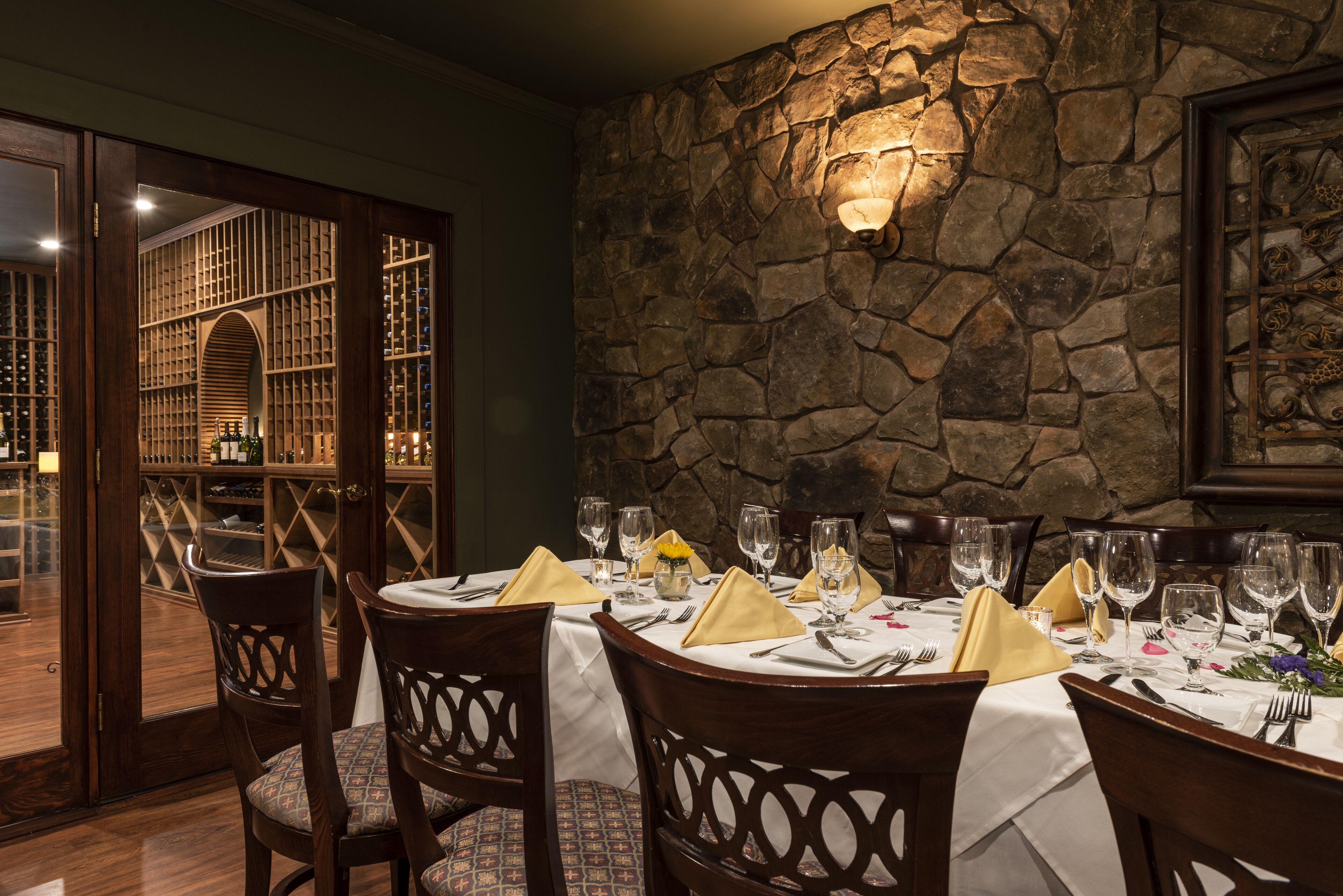 A dining area with a stone wall, wooden chairs, and a table set for a meal.