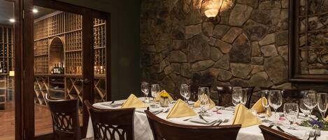A dining area with a stone wall, wooden chairs, and a table set for a meal.