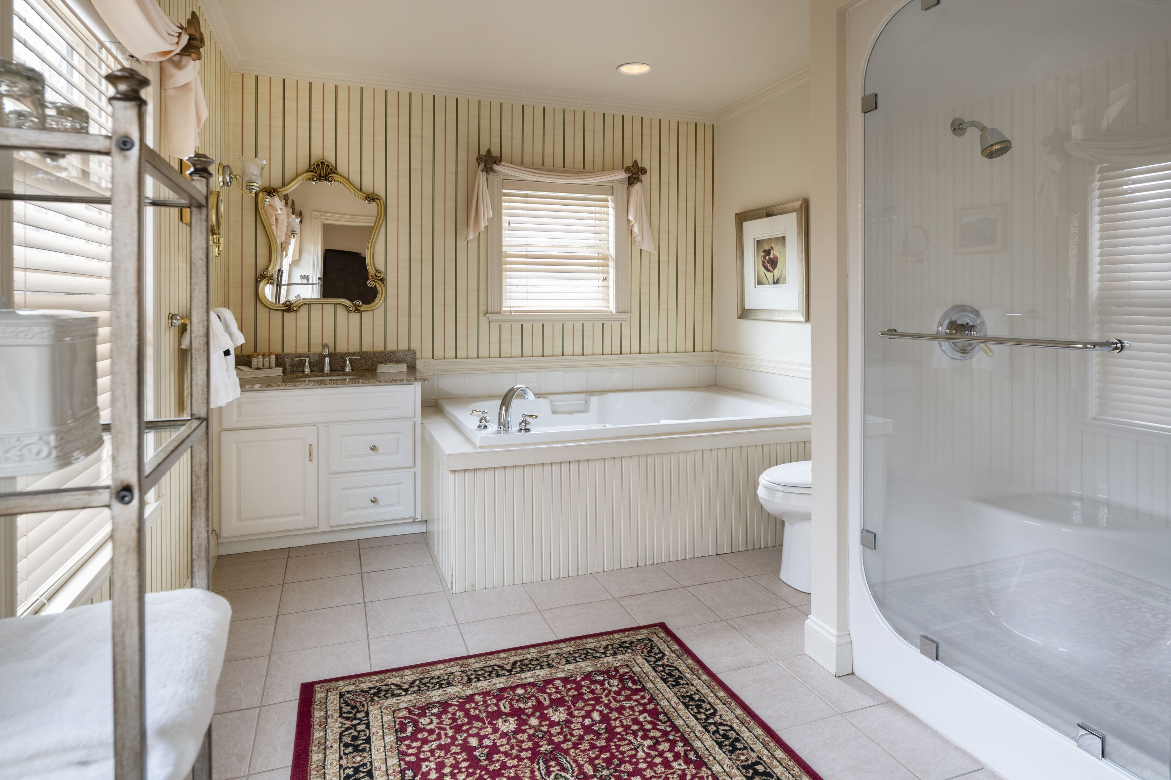 A bathroom with a bathtub, a sink, and a toilet. There is a window with blinds and a mirror above the sink.