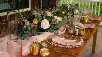 A table set with pink linens, gold cutlery, and clear glassware, surrounded by a floral centerpiece.