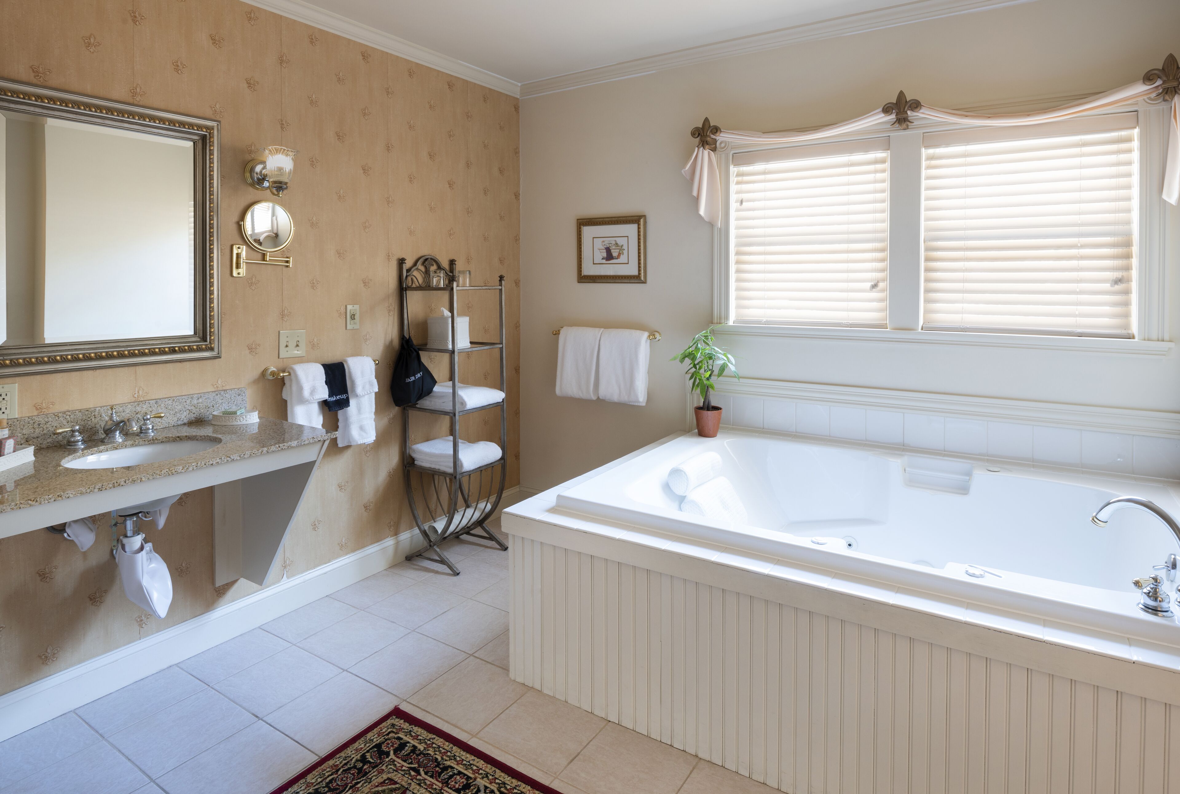 Une salle de bain dotée d’une grande baignoire, d’un meuble-lavabo à deux vasques, d’un miroir et d’une fenêtre avec des stores.
