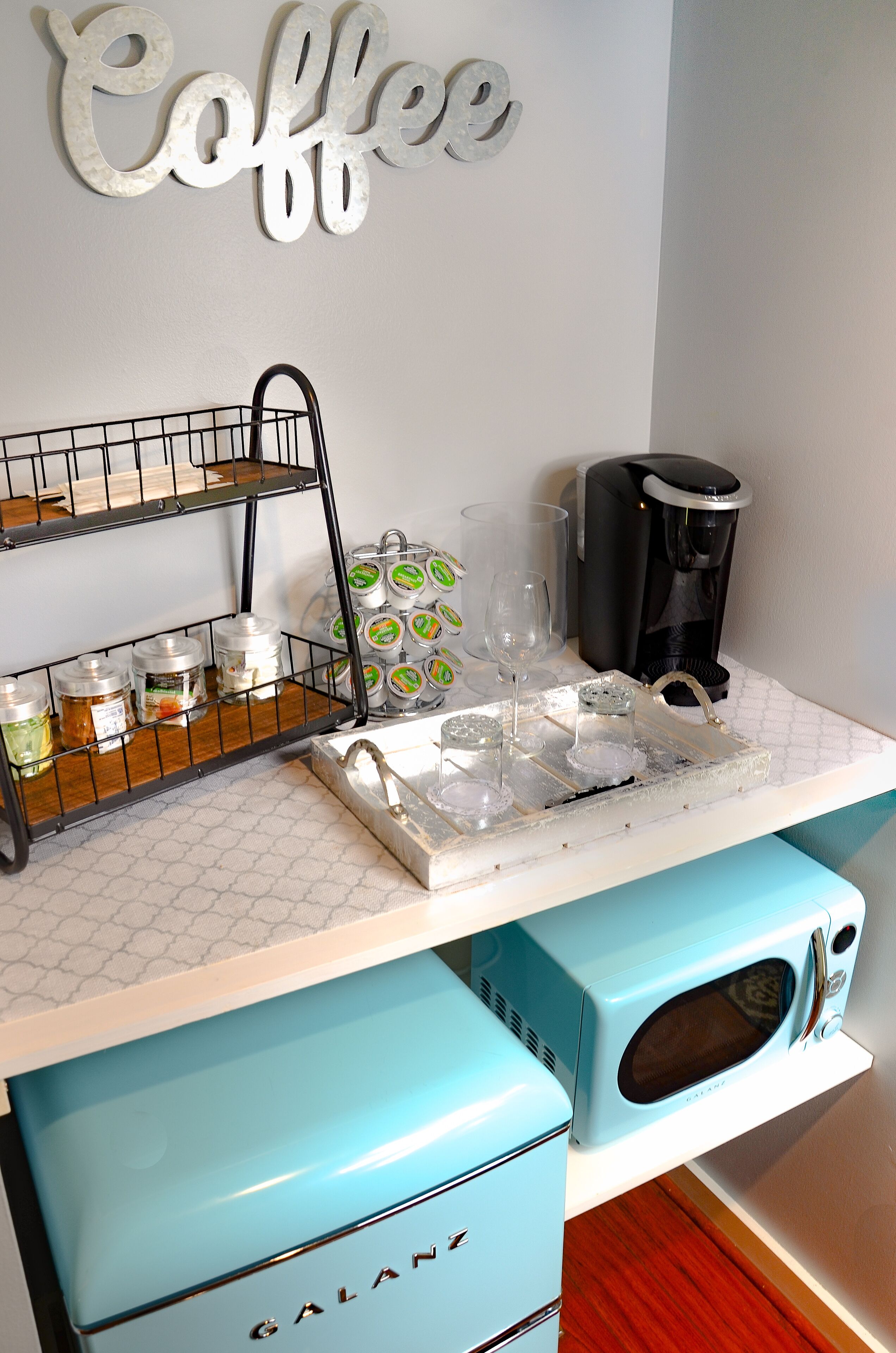A kitchenette with a coffee station, including a coffee maker, jars, and a tray with glasses.