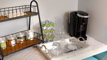 A kitchenette with a coffee station, including a coffee maker, jars, and a tray with glasses.