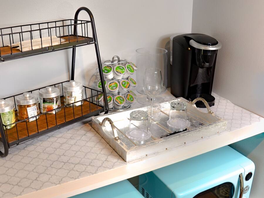 A kitchenette with a coffee station, including a coffee maker, jars, and a tray with glasses.