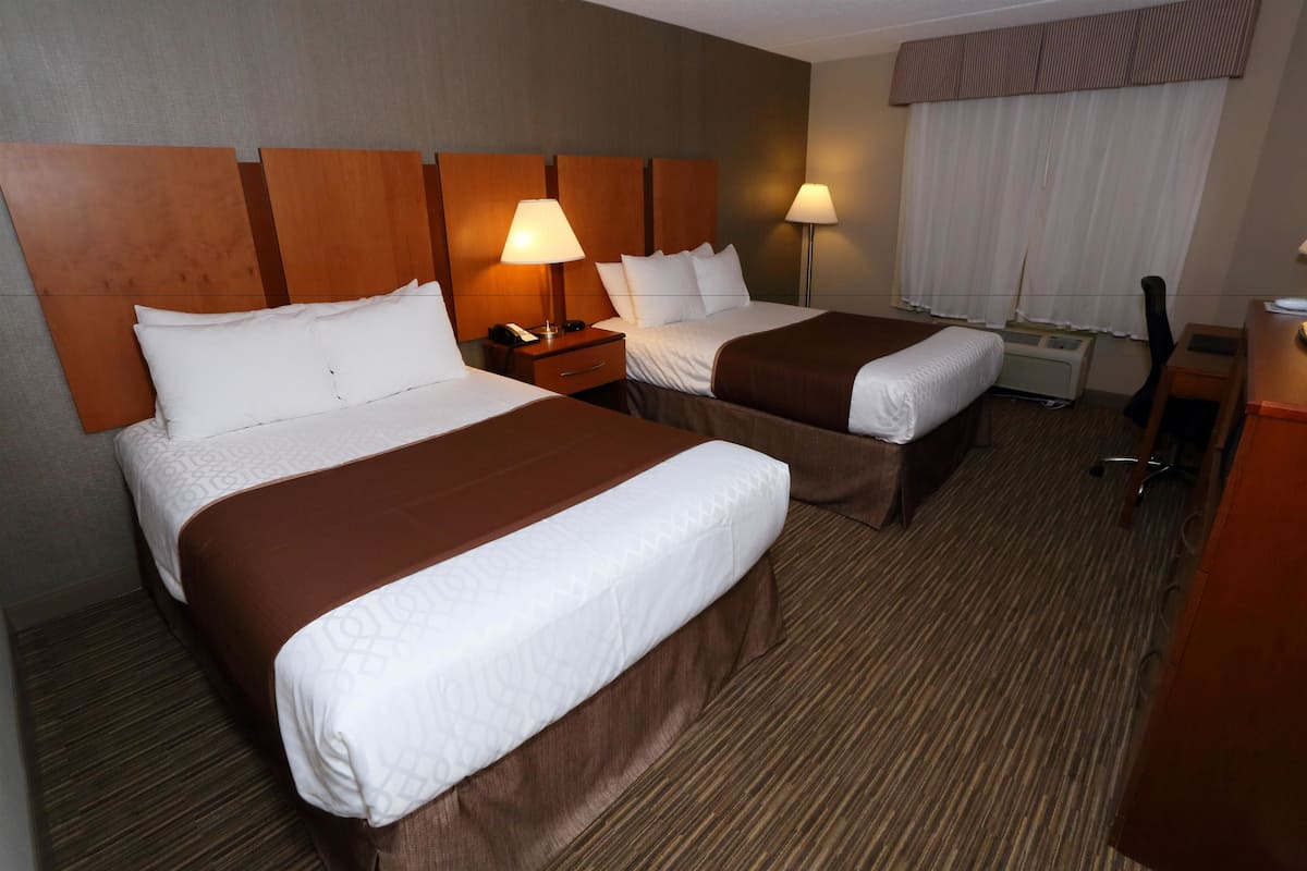 Ein Hotelzimmer mit zwei Betten, einem Schreibtisch, einem Stuhl und einer Lampe.