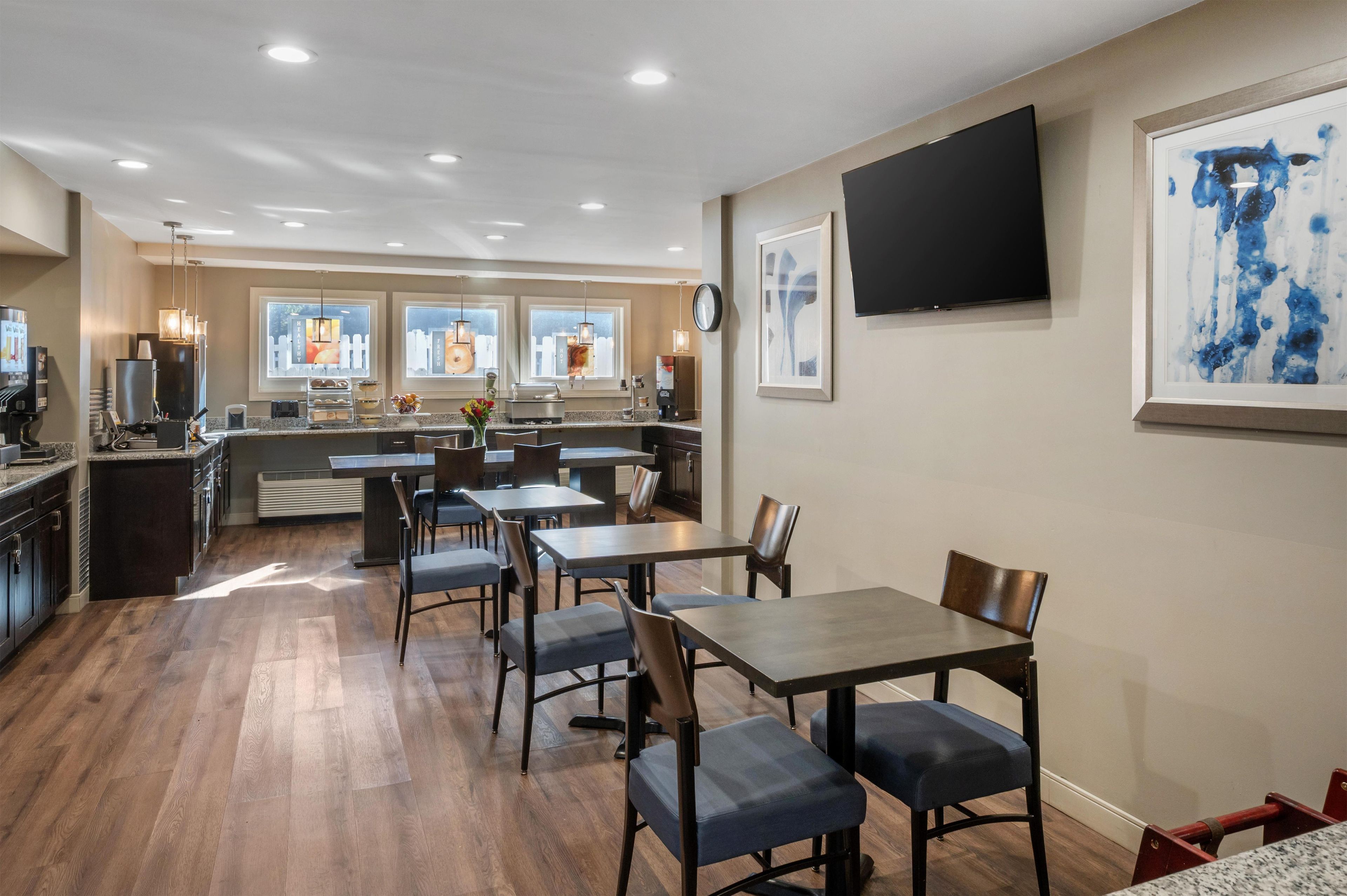 A modern dining area with tables and chairs, a kitchen in the background, and artwork on the walls.