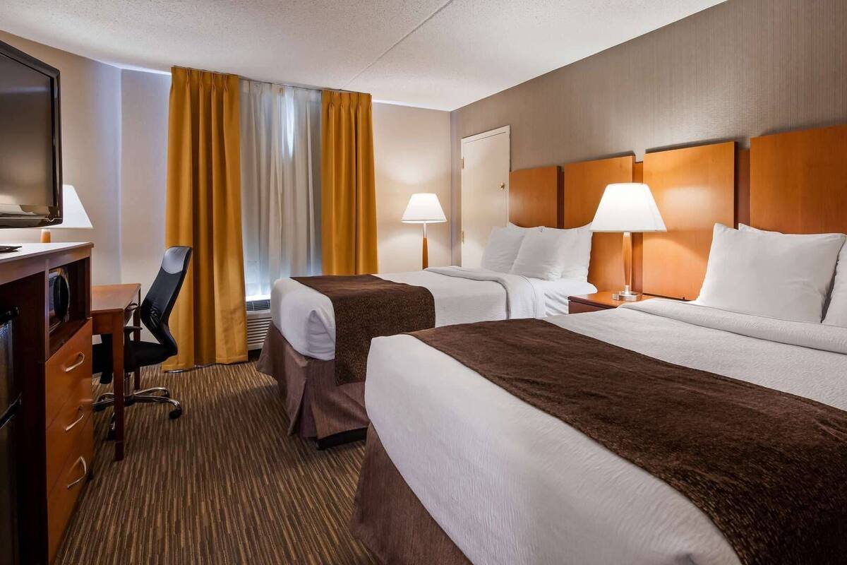 Ein Hotelzimmer mit zwei Betten, einem Schreibtisch, einem Stuhl, einem Fernseher und zwei Lampen.