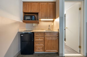 Una cocina compacta con armarios de madera, microondas integrado, refrigerador y pileta.