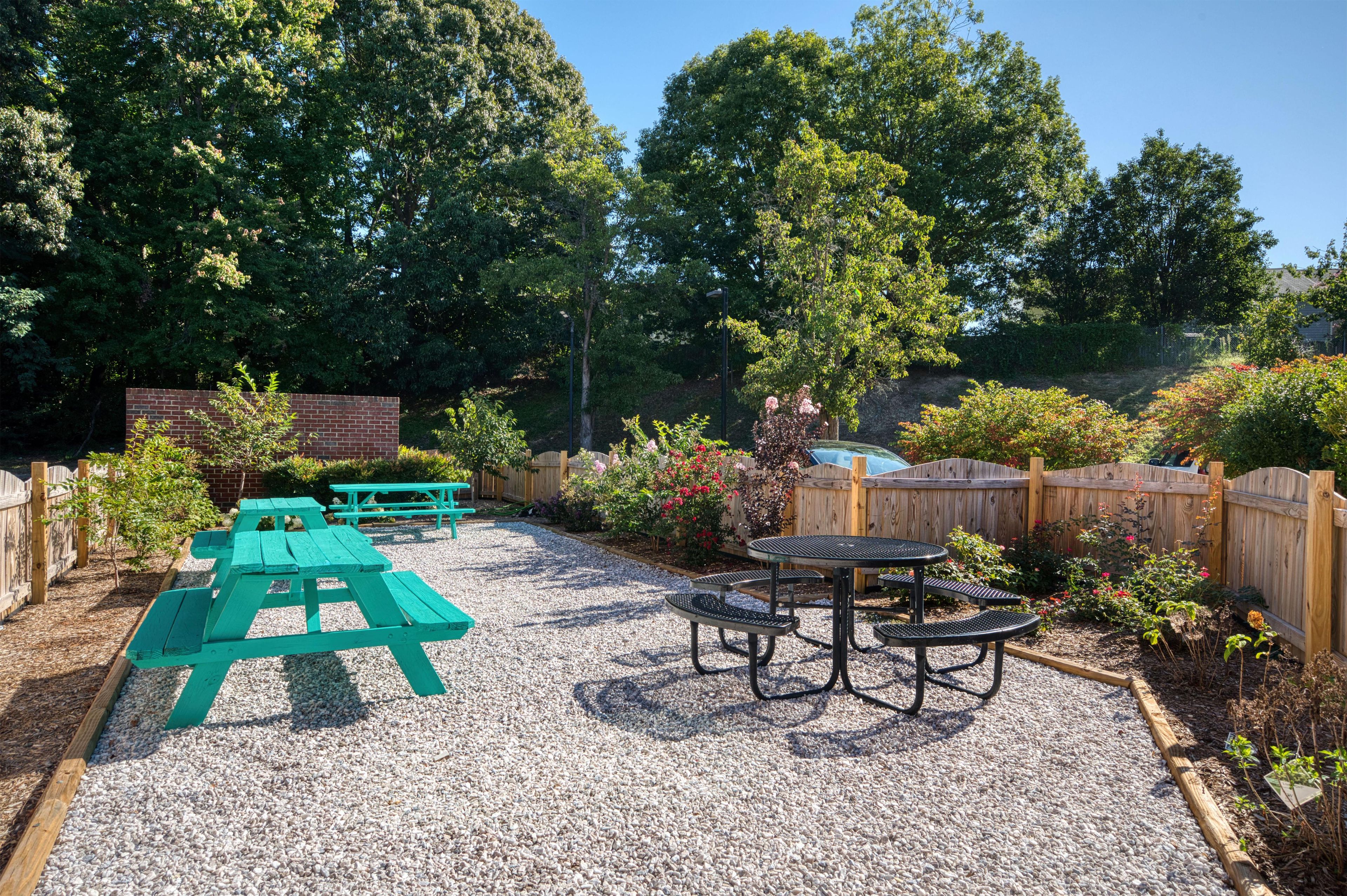 A gravel patio with picnic tables and a metal table surrounded by a wooden fence.