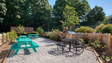 A gravel patio with picnic tables and a metal table surrounded by a wooden fence.