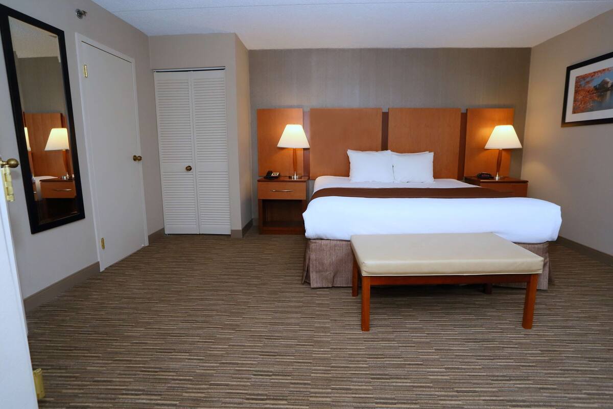 Ein Hotelzimmer mit Bett, Nachttischen, einer Bank, einem Spiegel und einer Tür.