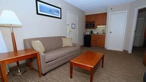 A hotel room with a sofa, a coffee table, a lamp, a framed picture on the wall, a microwave, and a refrigerator in the kitchen area. - Best Western La Plata Inn (La Plata)
