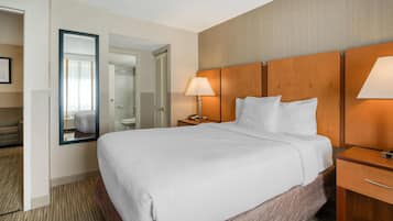 A hotel room with a large bed, a bedside table with a lamp, a mirror, and a view of the bathroom.
