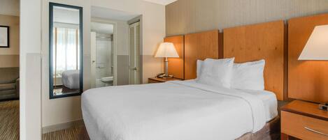 A hotel room with a large bed, a bedside table with a lamp, a mirror, and a view of the bathroom.