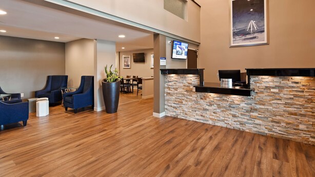 A reception area with a stone wall, blue chairs, a potted plant, and a flat-screen TV on the wall. - Best Western La Plata Inn (La Plata)