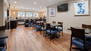 A modern dining area with wooden flooring, multiple tables and chairs, a kitchen area with a counter, and artwork on the walls. - Best Western La Plata Inn (La Plata)