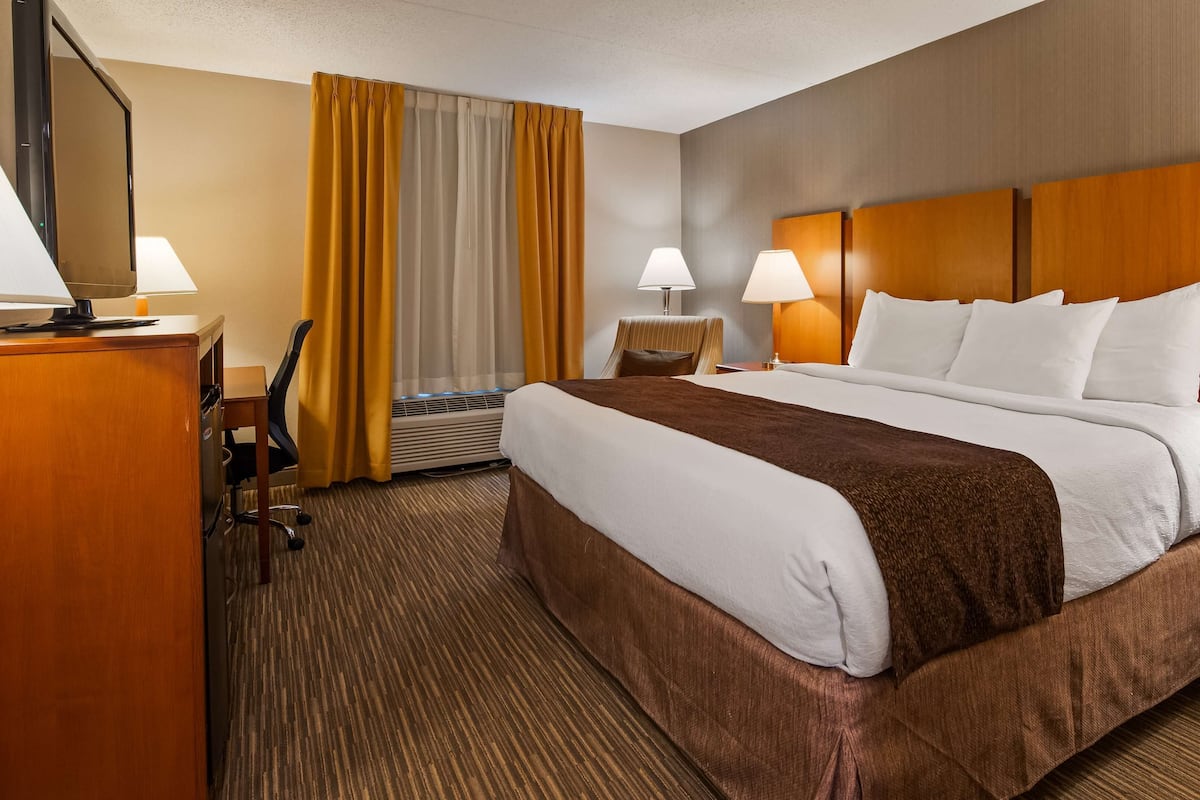 Ein Hotelzimmer mit einem großen Bett, zwei Nachttischen mit Lampen, einem Schreibtisch mit Stuhl und einem Fenster mit Vorhängen.