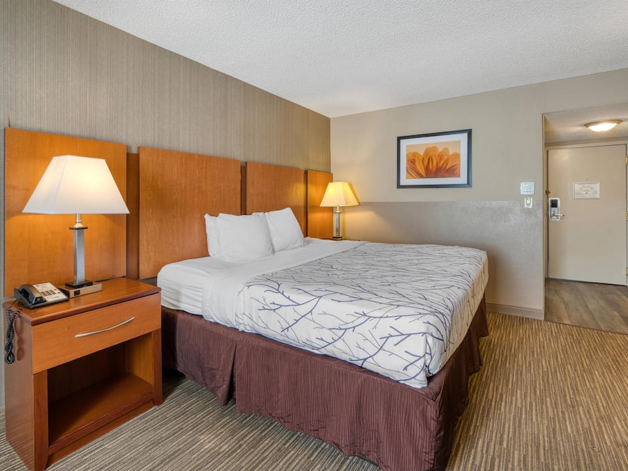 A hotel room with a bed, bedside lamps, a desk with a phone, and a door leading to another room.