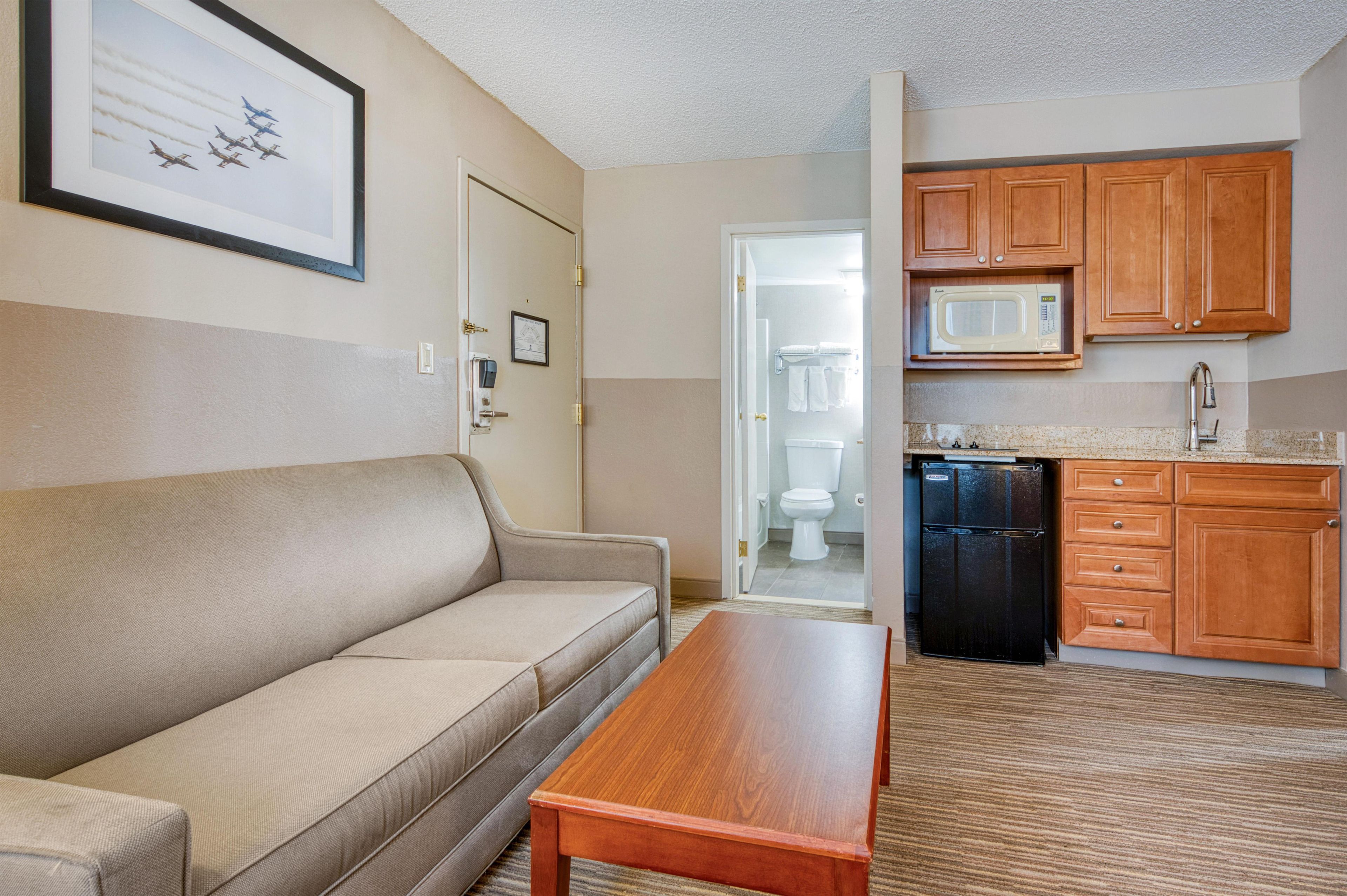 Un espacio habitable compacto con un sofá, una mesa de madera, una kitchenette con microondas y una puerta que da a un baño.