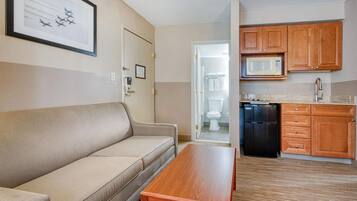 Un espacio habitable compacto con un sofá, una mesa de madera, una kitchenette con microondas y una puerta que da a un baño.