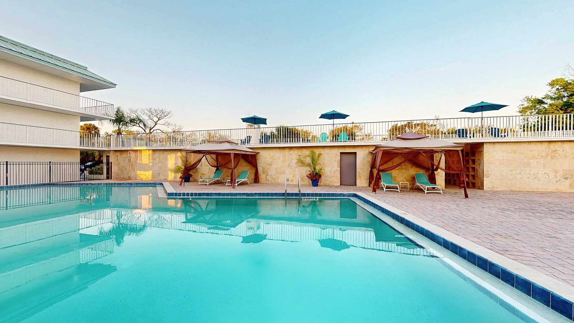 Een zwembad met ligbedden en parasols, omringd door een gebouw met een balkon.