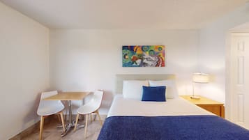Une chambre d’hôtel avec un lit, un bureau, deux chaises, un tableau au mur et une table de chevet avec une lampe.