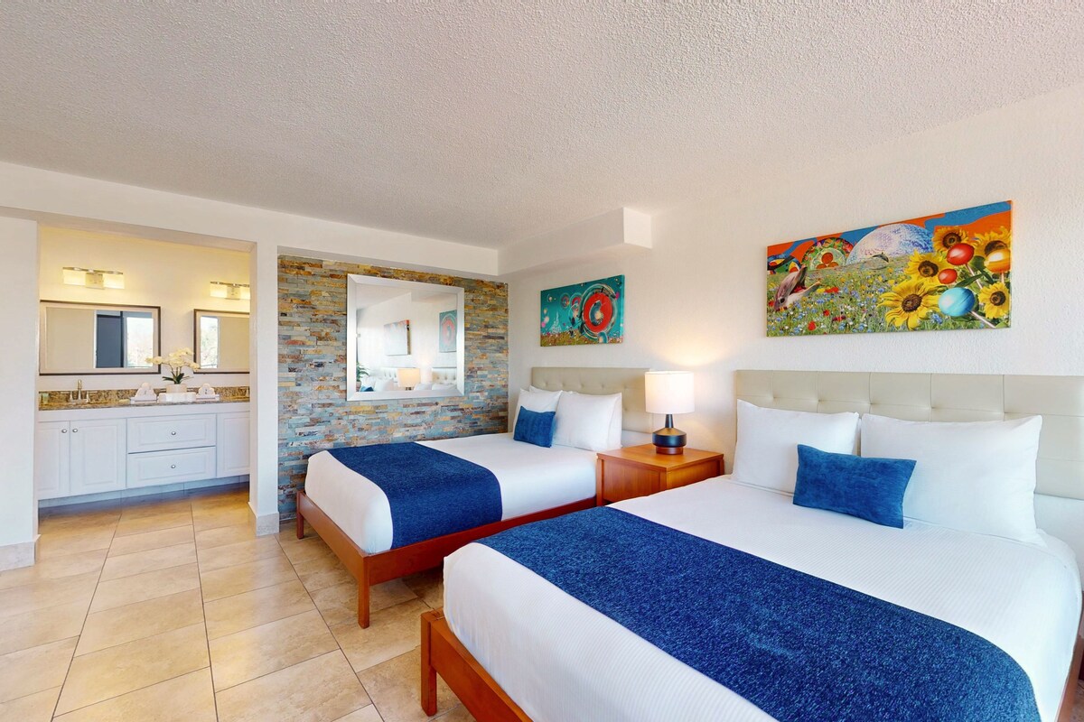 A hotel room with two beds, a bathroom, and a dining area.