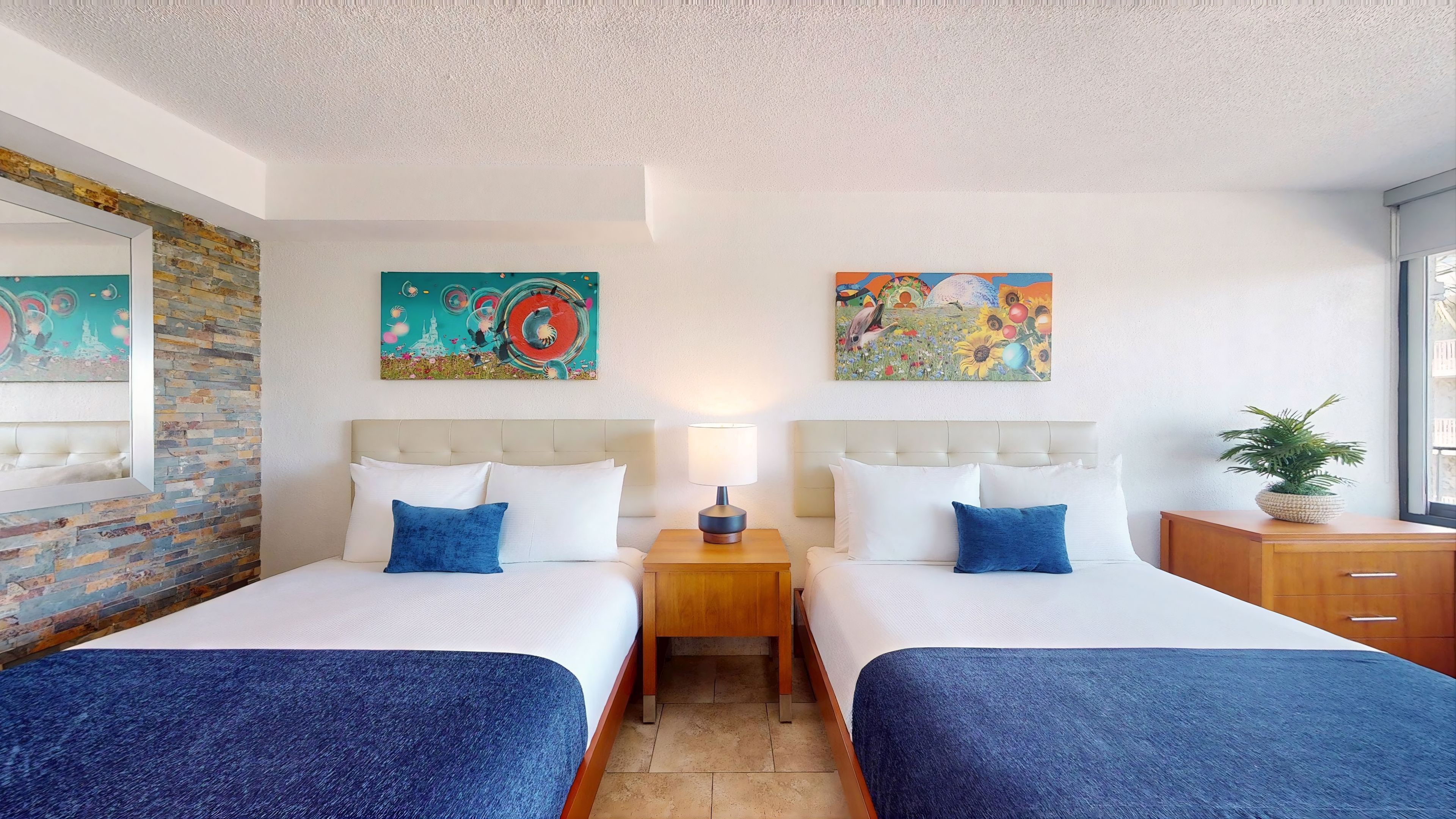Ein Hotelzimmer mit zwei Betten, einem Nachttisch, einer Lampe und Bildern an den Wänden.