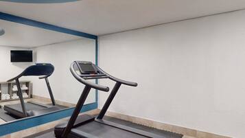 A gym with treadmills, a mirrored wall, and a television.