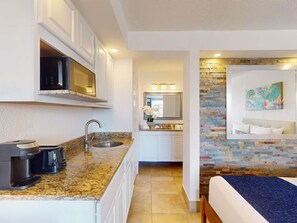 A compact hotel room with a kitchenette, a bed, a bathroom with a shower, and a living area with a painting. - Park Royal Orlando managed by Accor (Kissimmee)